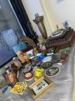 Wide view of assorted vintage men's knick knacks and bar ware items on cloth surface, showing diversity of items including figurines, metal bar accessories, mugs, and coasters.