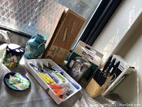 Photo showing various kitchenware including two Italian pottery vases with floral designs, mixed color cutlery set in plastic trays, and wooden knife block with knives.