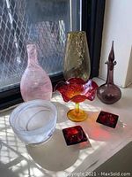 Photo showing all seven glass items together on a window sill with natural light.