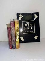 Four books standing and lying: two Harry Potter hardcovers with dust jackets, one Harry Potter paperback, and The Book of Magic hardcover with dust jacket