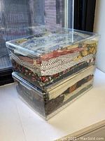 Two plastic bins stacked containing multiple vintage fabric pieces with various floral, polka dot, striped and geometric printed patterns in assorted colors.