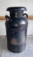 Front view of black painted steel milk can showing weathered label area and handles.