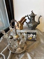 Photo showing antique silver plated cruet set with multiple crystal cut glass condiment bottles on a silver tray with handle, monogrammed quadruple plated teapot, wooden knife block with knives, and small condiments