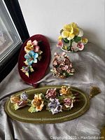 Four porcelain floral plaques on velvet and ceramic bases, arranged on silver cloth near window, showing details and colors