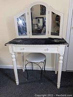 Front view of white vanity table with three mirrors and round stool underneath