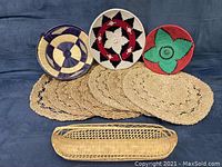 Photo showing three patterned round baskets and a long narrow basket arranged above a row of round straw placemats, highlighting variety and colors.