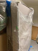 Side view of mattress and box spring stacked and covered in plastic.