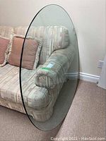 Clear round glass table top leaning against a patterned couch, showing full size and shape.