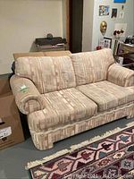 Front and angled view of a two-cushion sofa with rolled arms covered in patterned beige fabric