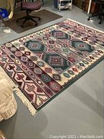 Full view of the rectangular carpet showing the overall geometric and diamond patterned design and the fringed ends.