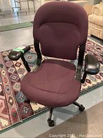 Front view of the dark purple cloth office chair with armrests and five legs caster base on a patterned rug.
