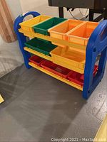 Blue plastic frame organizer holding yellow, green, orange, and red plastic bins arranged on three shelves.