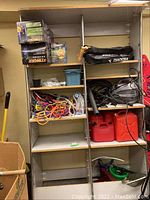 View of shelving unit with various stored items such as red fuel containers, extension cords, storage bins, and tools.