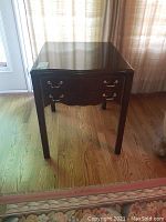 Front angled view of dark wood night table showing two drawers with brass handles and surface finish.