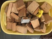 Yellow basket filled with solid wooden building blocks of various rectangular and square shapes, showing scratches and paint marks.