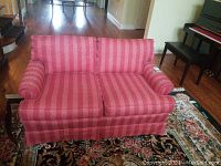 Red striped fabric upholstered loveseat in living room with floral rug and hardwood floor, showing front and slight side view