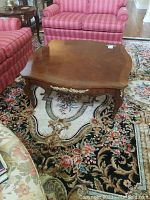 Front view of a wooden coffee table placed between red upholstered couches, highlighting the polished wood surface and brass decorative elements on the legs.