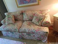 Front view of feather stuffed floral fabric sofa showing two-seat cushions and two matching decorative cushions on a patterned rug beneath a framed artwork.