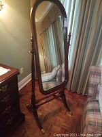 Full view of the cheval mirror showing the arched top glass and the supporting wooden frame with turned side posts and base.