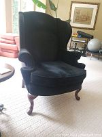 Front angle view of a black wing back armchair showing the seat, arms, and legs with some natural lighting.