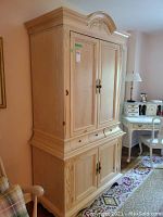 Full front view of the cream entertainment armoire showing double upper doors, middle drawers, and lower doors with carved accent details
