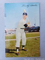 Front color image of Mickey Mantle in batting pose on baseball field with printed signature.