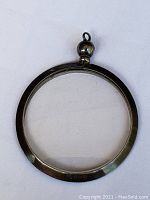 Top view of the round silver pendant locket showing smooth silver frame with patina and bail for hanging
