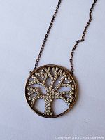Close-up of round Tree of Life pendant set with clear rhinestones on a silver-tone metal with a pinkish hue.