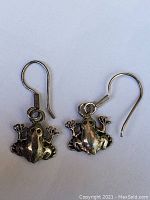 Pair of sterling silver frog-shaped dangle earrings with hook wire backs shown from front view on white background