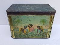 Front side of the tea box showing three figures harvesting tea leaves with palm trees behind them.