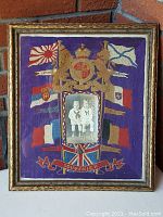 Full view of framed embroidered tapestry featuring multiple flags, royal coat of arms, and central photo of two boys in sailor suits.