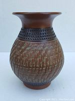 Front side view of the pottery vase showing bulbous body and textured carved pattern resembling basket weave.
