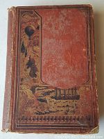 Front cover view showing red cloth with gilt embossing of balloon, cliffs, ship, ornate border
