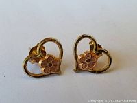 Pair of petite 14K gold earrings designed as open hearts with a daisy flower in the center, shown side by side on a white background.