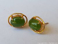 Pair of petite stud earrings each featuring an oval green jade cabochon set in a 14K gold prong setting with an open oval gold frame.