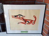 Framed artwork showing a stylized animal in Northwest Coast First Nations art style with black, red and beige colors against a cream background.
