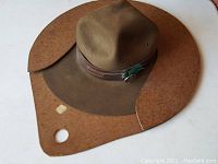 Front and top view of the brown vintage felt Boy Scouts hat placed on the leather shaped hanger.