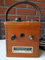 Front view showing wooden box with leather handle and front panel with input/output ports, rotary dial, toggle switch, and Foster Instrument Co Ltd label.