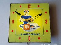 Top view of the square yellow clock face with red numbers and central genie figure logo.