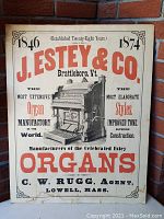 Full front view of an antique cardboard advertising poster for J. Estey & Co. organs, featuring large red lettering and detailed organ illustration.