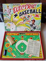 Full view of the electric baseball game board inside the box showing batteries, instruction sheet, and game controls.