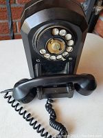 Front view of the black Bakelite rotary dial phone with the handset resting on the cradle, showing the rotary dial with letter and number markings.