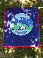 Front view of large indigenous-style tapestry with polar bear, fish, mountains, and celestial bodies in circle design on blue background with red border.