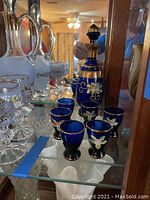 Photo showing the full set of cobalt blue glass decanter with stopper and six matching glasses with floral and gold detailing.