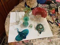 Full lot overview showing all six Murano glass items on a white base: two vases, a red decorative bowl, a stingray figurine, a green/white figurine, and an egg-shaped piece.