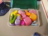 Various colored plastic craft punches in shapes such as flower, butterfly, heart, and spiral, stored in a transparent container.