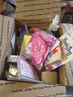 Box with various crafting supplies including Masking Magic masking product, pink stencil tool, spray cleaner bottle, and small packaged items.