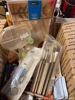 Photo of assorted scrapbooking punches with glitter effects, clear crafting tools, paintbrushes, and boxed photo pack inside a cardboard shipping box.