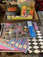 Overall view of box containing assorted scrapbooking supplies including embellishments, stickers, and patterned papers.