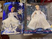Two Walt Disney Cinderella Holiday Princess Barbie dolls in original boxes. Both boxes show some damage and wear. Dolls dressed in white holiday attire with snowflake patterns.